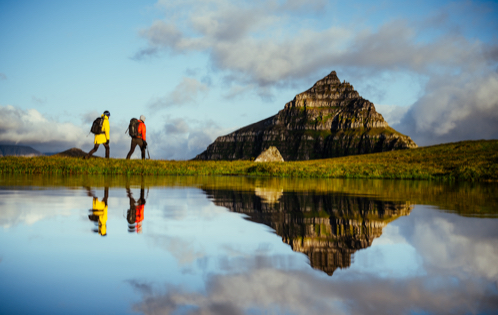 Man in a orange jacket hiking, with a low angle showing a small lake