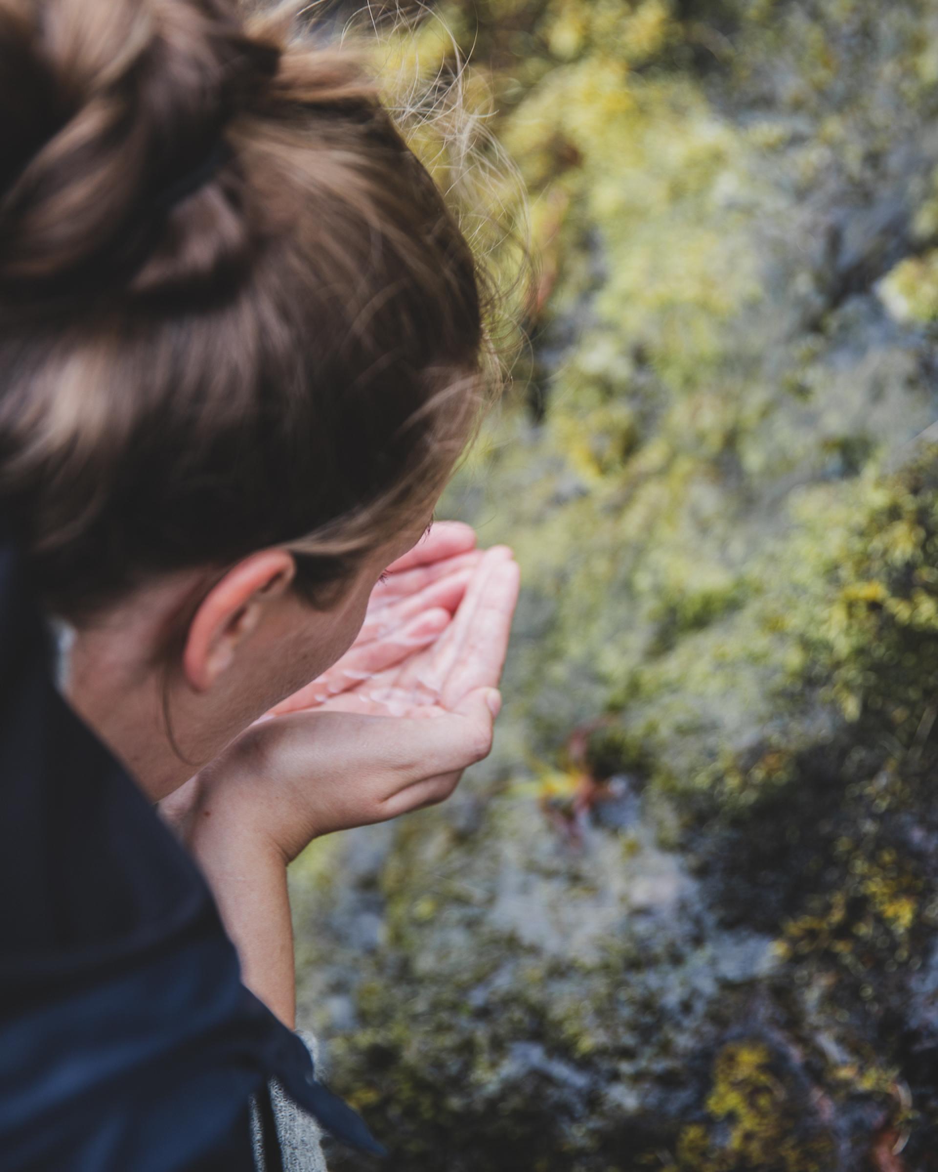 Girl drinking water from a pond in the mountains. Elduvík in the Faroe Islands. 